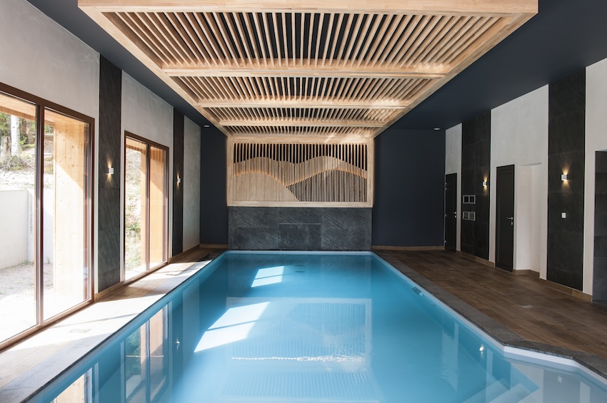 Photo d'une piscine intérieure avec un sol bois et des aménagements décoratifs en bois brut au plafond et sur les murs.